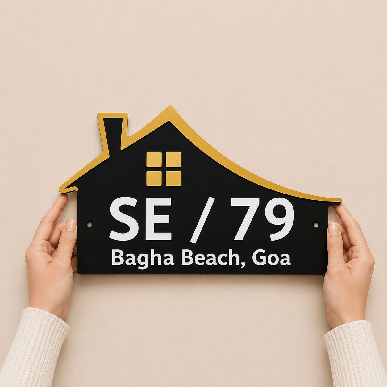 Hands holding a house shaped black acrylic name plate with gold mirror roof and white embossed letters