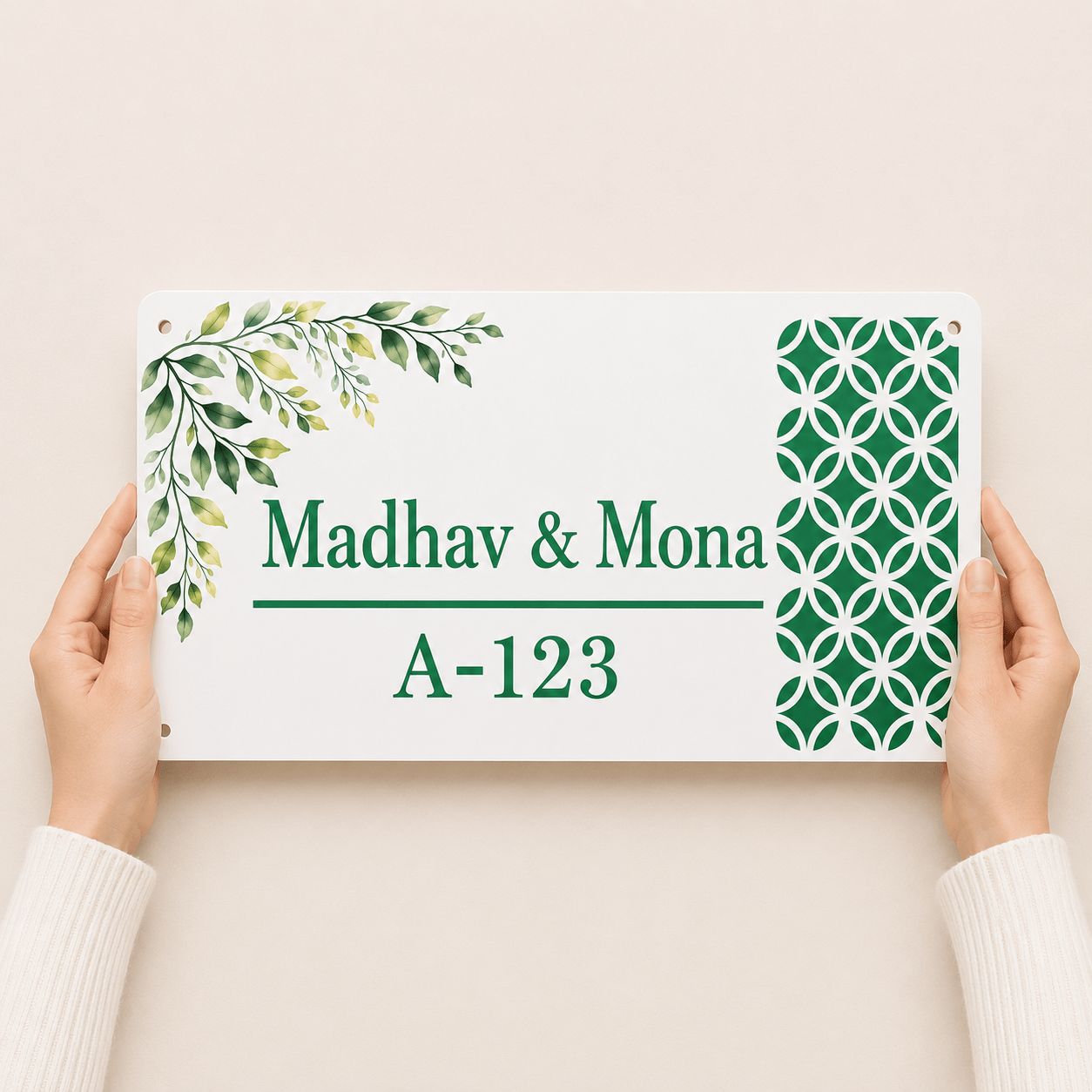 Hands holding a white acrylic couple name plate with green botanical leaf and abstract circle pattern